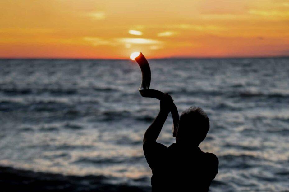 man blowing shofar on beach with sunset